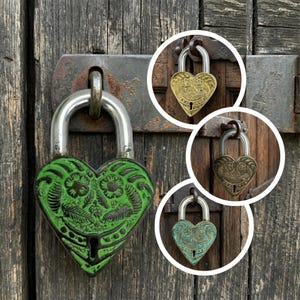 May include: A collection of heart-shaped padlocks in various colors and finishes. The main padlock is green with floral detailing, while the smaller ones are gold, bronze, and teal. The locks are mounted on a weathered wooden door.