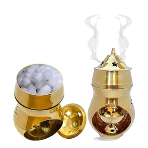 May include: A golden brass incense burner with a star-shaped lid and a small oil lamp inside. The burner is emitting smoke. Beside it is a golden bowl filled with white incense and a separate lid with star cutouts. The items are on a white background.