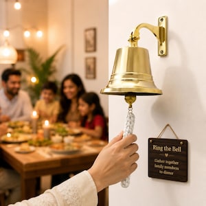 Pode incluir: Um sino de parede em lat&atilde;o polido com um puxador de corda tran&ccedil;ada branca. Abaixo do sino, pendura-se uma placa retangular de madeira escura com o texto "Ring the Bell" e "Gather together family members to dinner" gravado em cor clara.