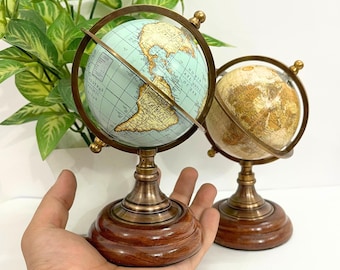 May include: Two decorative globes with brass meridian rings and stands. One globe features a light blue ocean and tan continents, while the other has a tan and brown color scheme. Both globes sit on a dark wooden base.
