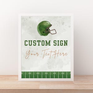 Op de afbeelding: Een ingelijste print met een groene American footballhelm. De tekst "CUSTOM SIGN" is groen, met "Your Text Here" in cursief. Onderaan de print staat een American footballveld-afbeelding.