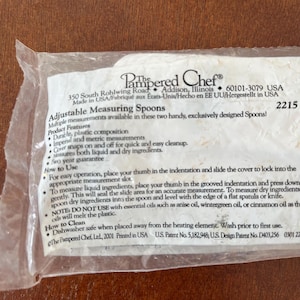 May include: A package containing The Pampered Chef adjustable measuring spoons. The package includes product features, how to use instructions, and cleaning instructions. The spoons measure both liquid and dry ingredients.