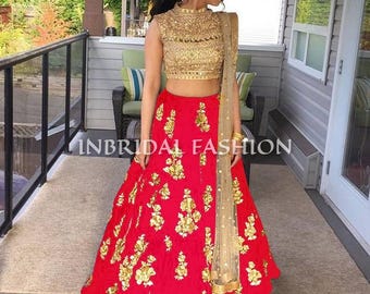 May include: A red lehenga skirt featuring gold floral embroidery paired with a matching gold sleeveless crop top with intricate beadwork and a sheer gold dupatta. The text INBRIDAL FASHION is visible across the center of the image.