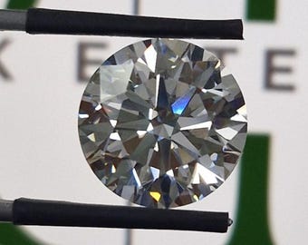May include: A round, brilliant-cut diamond held by tweezers. The diamond sparkles with numerous facets, reflecting light. The background features the text "ERK ENTERPRISES" in green and white.