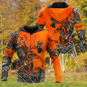 May include: An orange and camouflage hoodie featuring a deer design. The hoodie has a black hood and sleeves with the words "Name" and "Deer" on the sleeves. The deer design is in orange and black.