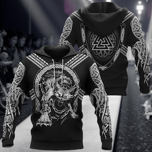 Könnte beinhalten: Schwarzer Hoodie mit Wolfsgrafik auf der Vorderseite und Schilddesign auf der Rückseite. Die Ärmel und die Kapuze weisen weiße keltische Knotenmuster auf. Der Wolf ist in einem kreisförmigen Rahmen.