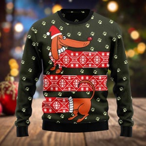 Könnte beinhalten: Grüner Weihnachtspullover mit einem Dackel, der einen Weihnachtsmannhut trägt. Der Pullover hat ein rot-weißes Schneeflockenmuster und Pfotenabdrücke. Die Ärmel und der Saum sind schwarz.