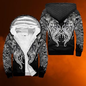 Könnte beinhalten: Schwarz-weißer Viking-Themen-Kapuzenpullover mit Reißverschluss und detaillierter Grafik eines bärtigen Kriegers. Der Hoodie hat ein weißes, flauschiges Innenfutter und ein gemustertes Design auf Kapuze und Ärmeln.