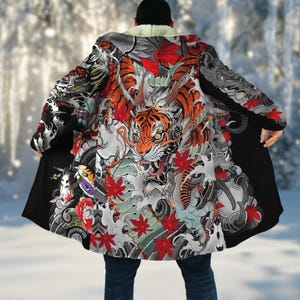 May include: A black coat with a vibrant Japanese-style tiger and dragon design. The coat features a white sherpa lining at the collar and a detailed illustration with red maple leaves and water elements. The coat is worn over dark blue jeans.