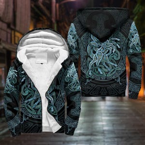 May include: Black zip-up hoodie with a white, fluffy interior lining. The exterior features a detailed teal and gray Celtic knot design, with a large circular pattern on the back and front. The hood displays a hammer symbol.
