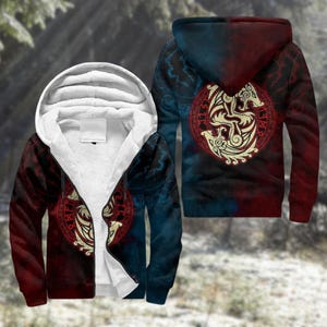 Puede incluir: Chaqueta con capucha y cremallera en rojo y azul, con interior forrado de sherpa color crema. La chaqueta presenta un diseño circular con dos pájaros estilizados en un círculo rojo en la espalda y en la parte delantera. El diseño tiene un tema vikingo.