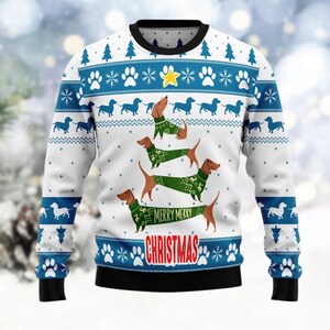 Könnte beinhalten: Weißer Weihnachtspullover mit schwarzem Kragen und Bündchen. Der Pullover hat blaue und weiße Schneeflocken- und Pfotenabdruckmuster mit Dackeln, die grüne Pullover tragen. Die Worte "MERRY MERRY CHRISTMAS" sind rot dargestellt.