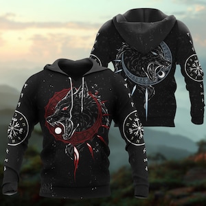 Puede incluir: Sudadera con capucha negra con un diseño de lobo con ojos rojos y un marco circular rojo. El diseño incluye una luna blanca y símbolos vikingos en las mangas. El fondo es una escena de noche estrellada.