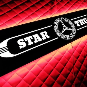 Puede incluir: Letrero rectangular negro con las palabras "STAR" y "TRUCK" en blanco, junto con el logotipo de Mercedes-Benz. El letrero está iluminado con un resplandor rojo sobre un fondo rojo con patrón de diamantes.