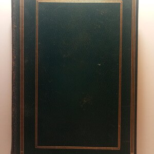 May include: A dark green book with gold trim. The cover is a solid dark green with a gold border and gold lines. The book appears to be old, with some wear and tear visible on the edges.