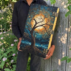May include: A large rectangular book with a dark cover featuring a stylized tree silhouette against a glowing orange moon and a deep blue starry sky. The book has three antique brass-colored metal latches along the side and visible page edges.