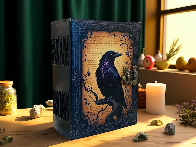 May include: A dark blue, leather-bound journal with a raven illustration. The raven is perched on a branch against a parchment-style background. The journal has a metal clasp and decorative frame.