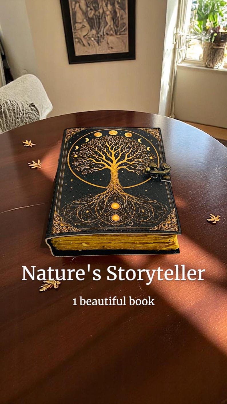 May include: A black journal with a gold tree of life design and the text "Nature's Storyteller". The journal has a clasp closure and gold-colored edges. The book is on a dark brown wooden table.