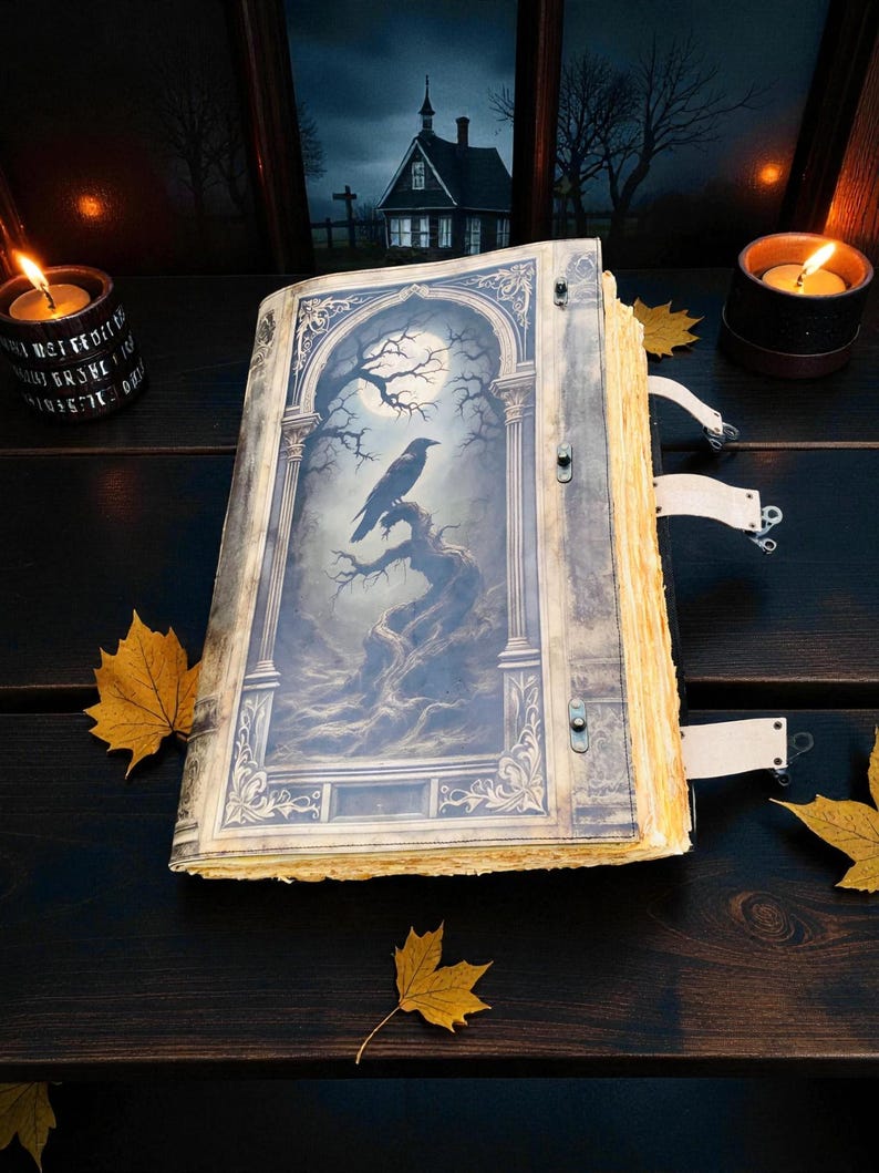 Op de afbeelding: Een open boek in antieke stijl met een gedetailleerde illustratie van een raaf die op een tak zit onder een volle maan. Het boek heeft verouderde, vergeelde pagina's en decoratieve sluitingen. Herfstbladeren en brandende kaarsen omringen het boek en cre&euml;ren een gotisch thema.