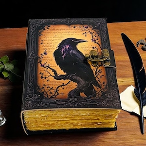 May include: A leather-bound journal with a raven illustration. The cover features a black raven perched on a branch against a parchment-like background. The journal has a metal clasp and aged, yellowed pages. A black feather quill and ink bottle are nearby.