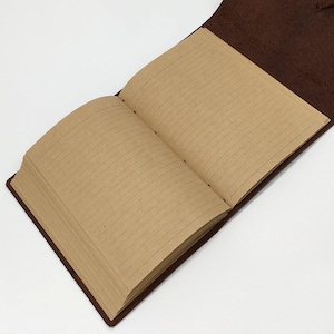 May include: An open, brown leather journal with lined, tan-colored pages. The journal is lying open, revealing the interior pages. The cover is a darker shade of brown, and the pages are neatly bound.