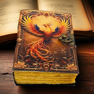 May include: A leather-bound journal with a detailed phoenix illustration on the cover. The phoenix is depicted with vibrant orange, yellow, and blue feathers. The journal has a brass clasp and gilded page edges, suggesting a vintage or fantasy theme.