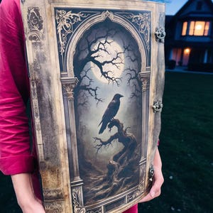 Op de afbeelding: Een groot, decoratief boek met een gotische illustratie van een raaf op een tak onder een volle maan. Het boek heeft sierlijke goudkleurige metalen sluitingen en een gedetailleerde, verouderde uitstraling, wat wijst op een vintage- of fantasiethema.