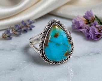 May include: A silver ring featuring a large, pear-shaped turquoise stone with brown matrix veins. The stone is set in a twisted rope-style silver bezel, and the band consists of a split-shank design, showcasing a polished metallic finish.