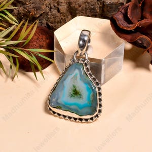 May include: A silver pendant with a triangular, blue and green agate stone. The stone has a unique pattern with shades of blue and green. The pendant has a silver bail for attaching to a chain. The jewelry is displayed on a neutral surface.