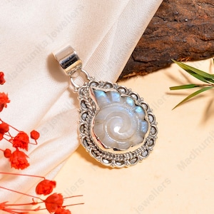 May include: A silver pendant with a pear-shaped design, featuring a white and blue gemstone carved in a spiral pattern. The pendant has a decorative, ornate border and a silver bail for a chain.