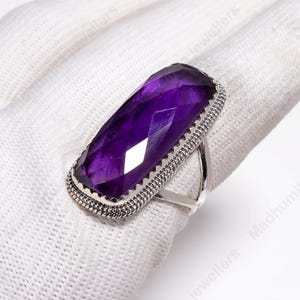 May include: A silver ring with a large, rectangular, faceted amethyst gemstone. The amethyst is a deep purple colour and is set in a detailed silver setting. The ring's band is a simple, polished silver.