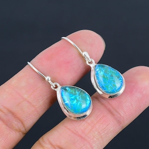 Puede incluir: Un par de pendientes plateados con forma de lágrima y piedras iridiscentes azules y verdes. Los pendientes tienen un diseño de gancho simple y un acabado pulido, mostrando las coloridas y llamativas piedras preciosas.