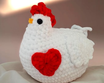 May include: A handmade, white crochet chicken with a red heart on its side. The chicken has a red comb and wattle, a yellow beak, and a black eye. The craft is made of soft yarn.