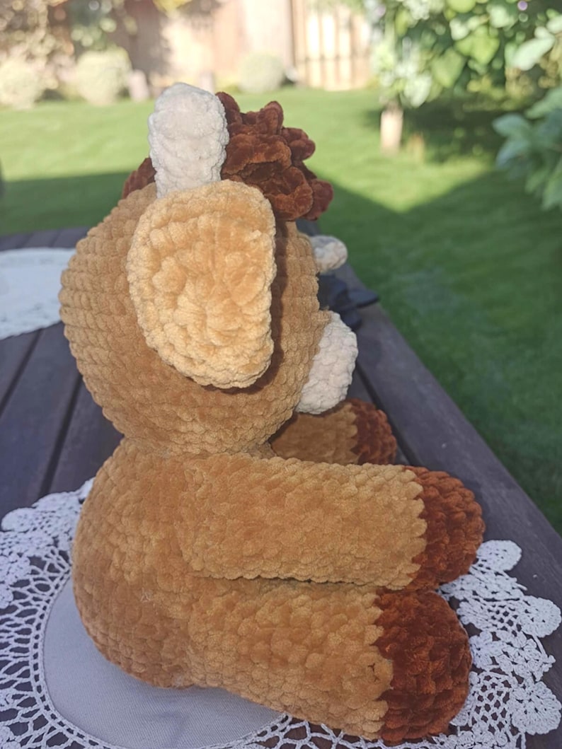 May include: A handmade plush toy in the shape of a deer, featuring a soft, textured fabric in shades of brown, tan, and cream. The deer has large ears, a fluffy mane, and a detailed face, perfect for a child's room or nursery.