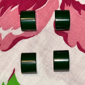 May include: Four dark green, rectangular, curved-edge objects are arranged on a floral patterned fabric. The objects have a glossy finish and appear to be made of a solid material.
