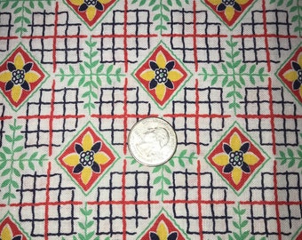May include: Close-up of a fabric with a repeating pattern. The design features red and navy blue grid lines, yellow and red diamond shapes with floral centers, and green leaf accents. A quarter coin is in the center.