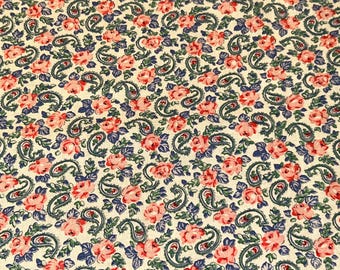 May include: Cream-colored fabric with a repeating pattern of pink roses, blue paisley shapes, and green leaves. The floral design is densely packed across the surface, creating a vintage aesthetic. The fabric is likely cotton or a similar material.
