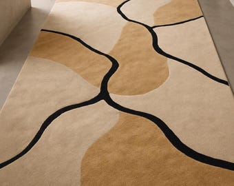 May include: A rectangular rug with an abstract design. The rug has a beige background with tan and light brown shapes, and black curved lines. The rug is made of a soft, plush material.