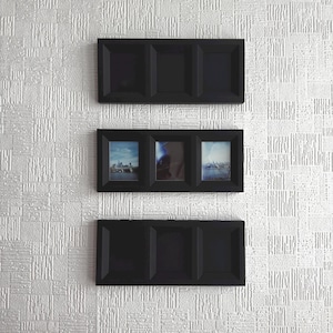 May include: Three black rectangular picture frames are mounted on a textured white wall. One frame contains three pictures of a city skyline. The other two frames are empty. The frames are evenly spaced vertically.