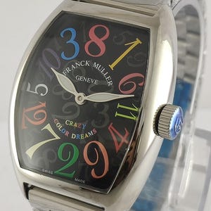 May include: A stainless steel Franck Muller Crazy Color Dreams watch. The black dial features colorful numerals and the words "CRAZY COLOR DREAMS". The watch has a silver band and a crown with a blue accent.