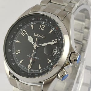 May include: A stainless steel Seiko watch with a black dial. The watch features a date display, luminous hands, and a compass bezel. The watch has a stainless steel band and two blue-accented crowns. The watch is an automatic model.