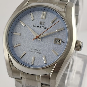 Pode incluir: Um relógio Grand Seiko em aço inoxidável com mostrador texturizado azul claro. O relógio apresenta um visor de data às 3 horas e uma pulseira prateada. O mostrador do relógio tem o texto "Grand Seiko" e "Automatic Hi-Beat 36000".