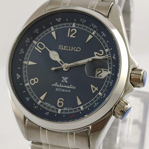 May include: A stainless steel Seiko watch with a dark blue face. The watch features a date display, luminous hands, and a stainless steel band. The watch is water-resistant to 20 bar.