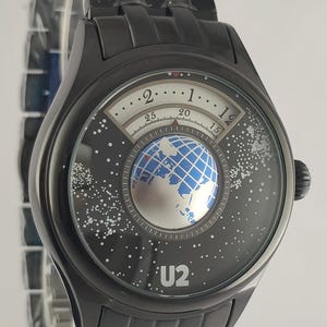 Puede incluir: Reloj de pulsera negro con un dise&ntilde;o &uacute;nico. La esfera del reloj presenta un gr&aacute;fico de globo terr&aacute;queo y el texto "U2". Tiene una correa de metal negro y una caja redonda negra. La esfera del reloj tambi&eacute;n tiene un dise&ntilde;o de noche estrellada.