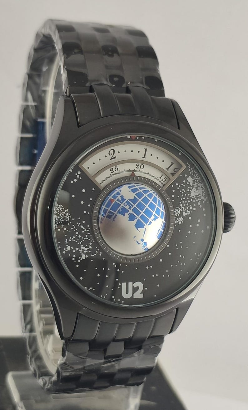 Puede incluir: Reloj de pulsera negro con un dise&ntilde;o &uacute;nico. La esfera del reloj presenta un gr&aacute;fico de globo terr&aacute;queo y el texto "U2". Tiene una correa de metal negro y una caja redonda negra. La esfera del reloj tambi&eacute;n tiene un dise&ntilde;o de noche estrellada.