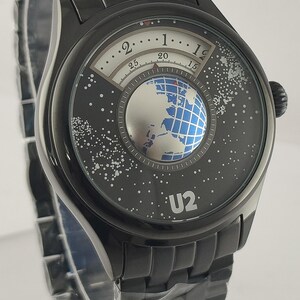 Puede incluir: Reloj de pulsera negro con una esfera &uacute;nica con un dise&ntilde;o de globo terr&aacute;queo y la banda U2. La esfera del reloj tiene un dise&ntilde;o blanco y negro con un globo plateado en el centro. La correa del reloj es negra.
