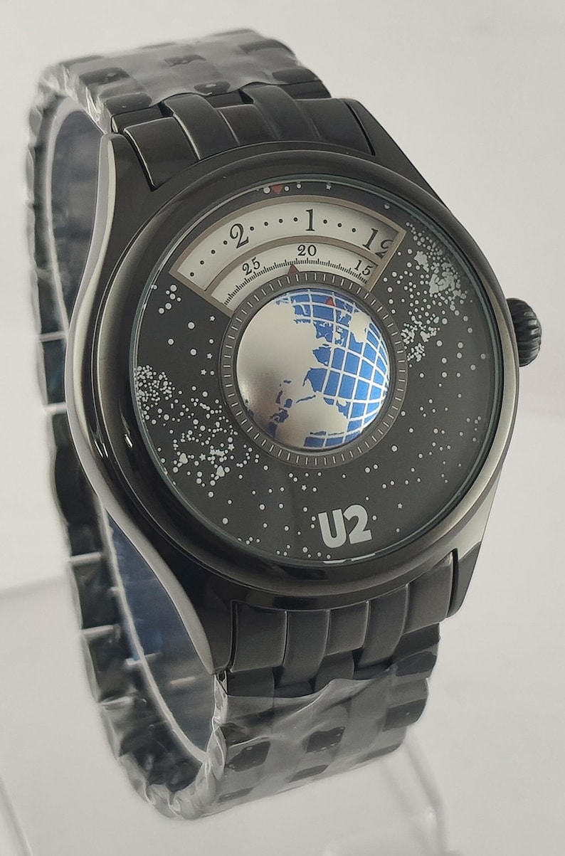Puede incluir: Reloj de pulsera negro con una esfera &uacute;nica con un dise&ntilde;o de globo terr&aacute;queo y la banda U2. La esfera del reloj tiene un dise&ntilde;o blanco y negro con un globo plateado en el centro. La correa del reloj es negra.