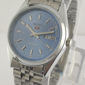 May include: A silver-toned wristwatch with a light blue face and a matching stainless steel band. The watch face displays the day and date, with the day reading "FRI 16". The watch has a round face with silver hands and markers.