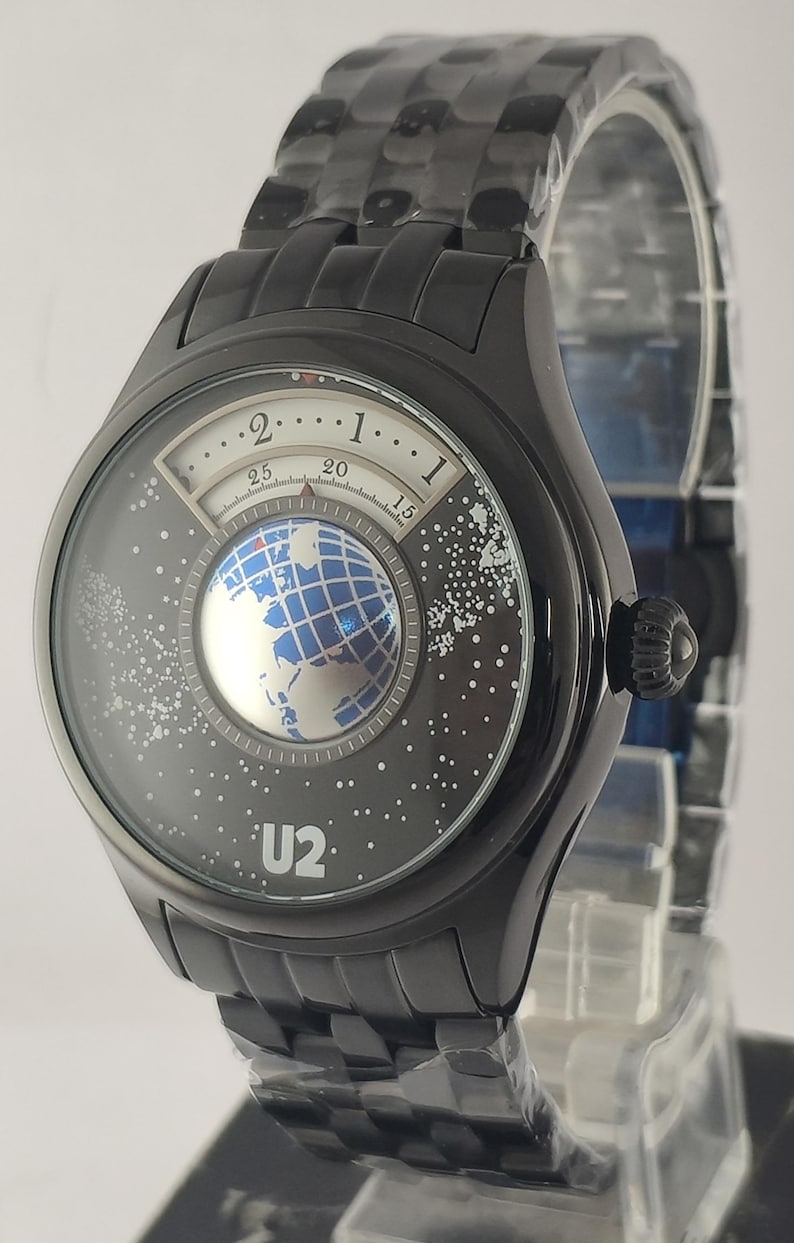 Puede incluir: Reloj de pulsera negro con una esfera &uacute;nica que presenta un dise&ntilde;o de globo terr&aacute;queo y el texto "U2". El reloj tiene una correa negra y una caja redonda negra. La esfera del reloj tiene un dise&ntilde;o de globo terr&aacute;queo blanco y azul.