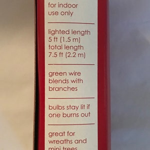May include: A red and white box with the words "holiday time" and information about a 7.5 ft (2.2 m) long string of lights. The lights are designed to blend with branches and have green wire. The box says the lights are great for wreaths and mini trees.